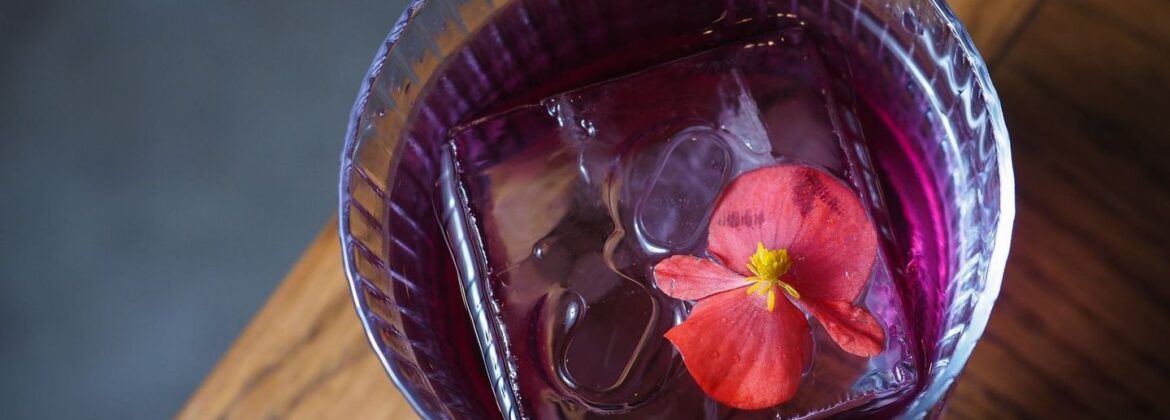 Paars drankje met ijs en bloem in een glas op een houten bar