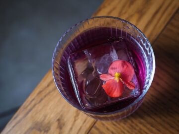 Paars drankje met ijs en bloem in een glas op een houten bar