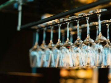 Rijen wijnglazen hangen ondersteboven aan een barrek